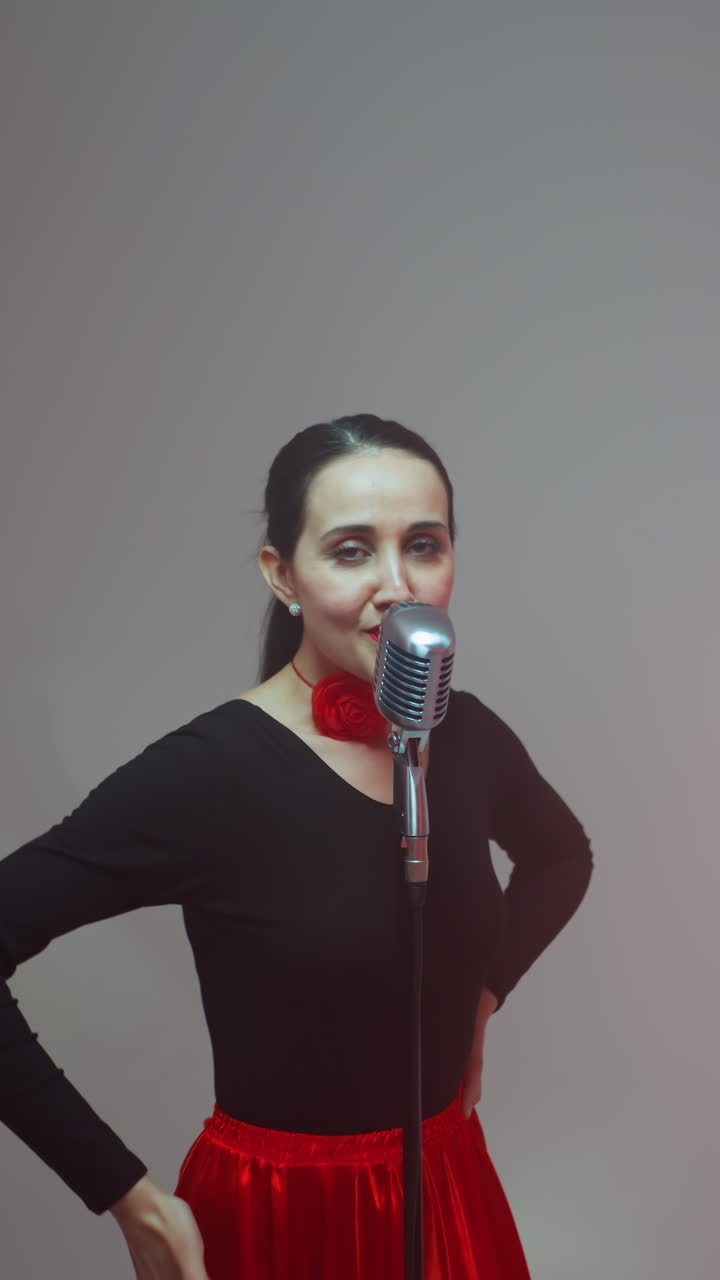 vocalista en una túnica negra y roja de pie frente a un micrófono vintage moviendo las manos lentamente, guitarrista tocando una guitarra roja, y tecladista tocando un sampler rojo contra un fondo gris