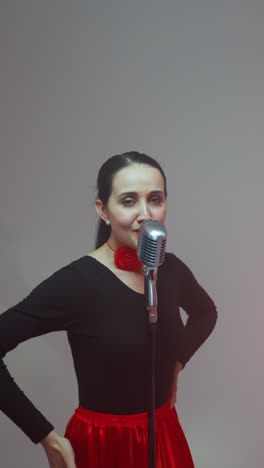 vocalista en una túnica negra y roja de pie frente a un micrófono vintage moviendo las manos lentamente, guitarrista tocando una guitarra roja, y tecladista tocando un sampler rojo contra un fondo gris