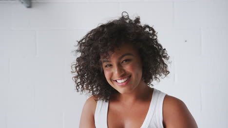 Retrato-De-Una-Mujer-Sonriente-Vestida-Informalmente-Con-Un-Chaleco-De-Pie-Contra-La-Pared-De-Un-Estudio-De-Ladrillo-Blanco