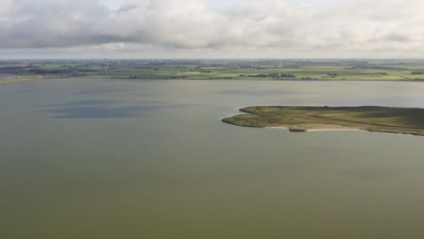 Aerial-shot-of-water,-farmland-and-Afsluitdijk-causeway-in-Kornwerderzand-in-Friesland,-the-Netherlands,-on-a-sunny-day