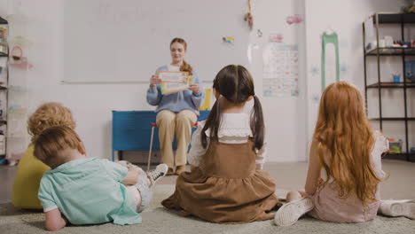 female teacher teaching words to her pupils whi are sitting on the floor in classroom in a montessori school