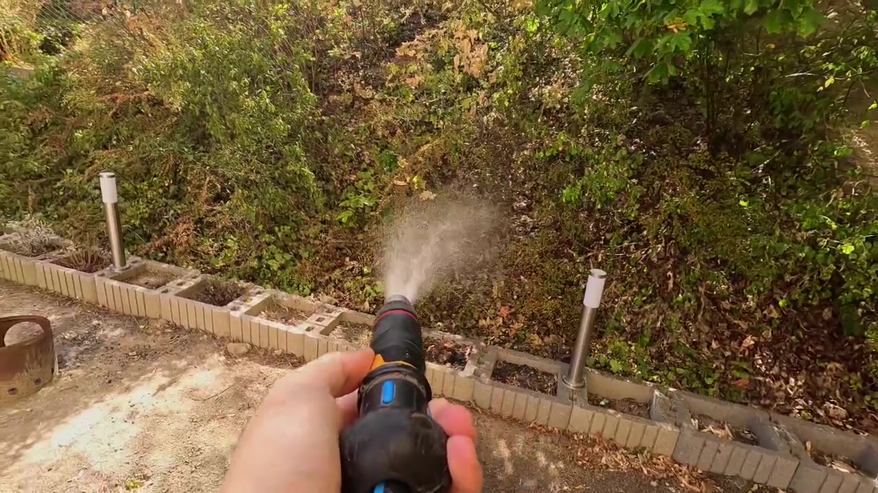 Ripresa in soggettiva di una persona che spruzza acqua con una canna da giardino su un pendio secco e pieno di foglie nel cortile di casa in una giornata di sole