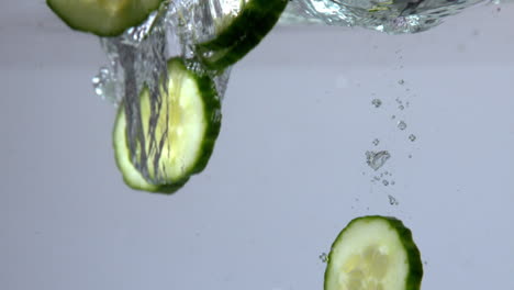 Courgette-slices-falling-in-water-on-white-background