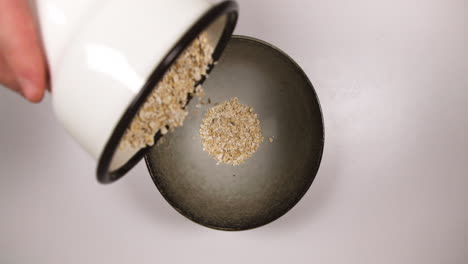 person pouring cup of rolled oats into a bowl for porridge