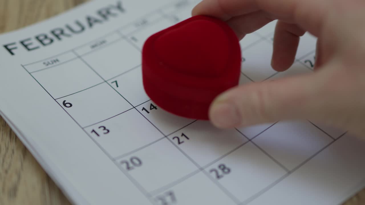 mano poniendo forma de corazón caja de anillo rojo en papel mes calendario 14 de febrero fecha