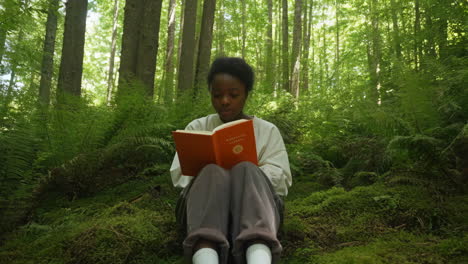 young woman reading a book in a lush green forest