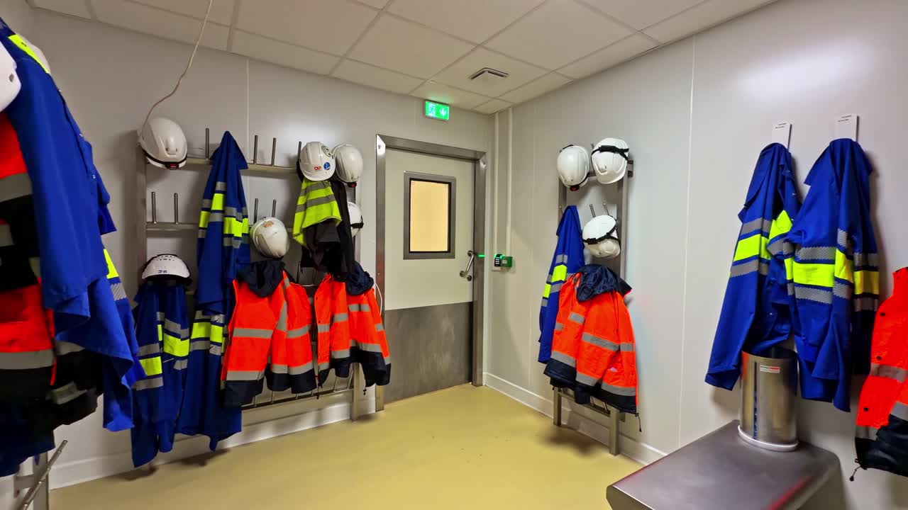 Spogliatoio industriale vuoto con giacche ad alta visibilità e cappelli appesi ai ganci, area spogliatoio pulita per DPI in una fabbrica o cantiere edile, deposito per attrezzature da lavoro e stazione per uniformi.