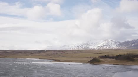 bright cloudy day with wet meadow and snowy mountain landscape, iceland