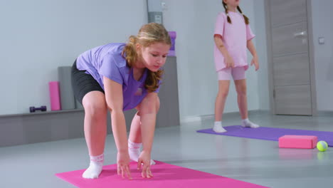 niñas jóvenes se involucran en un entrenamiento de movimiento hacia atrás, manteniendo el enfoque mientras están de pie rectas en esteras de ejercicio en un estudio de fitness brillante con equipos de gimnasia visibles en el fondo