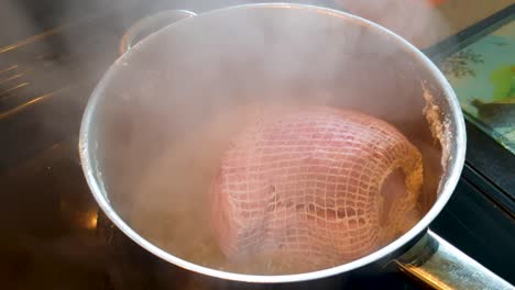 cured gammon hind leg of pork in netting simmering and cooking in a saucepan in the kitchen for sunday roast dinner