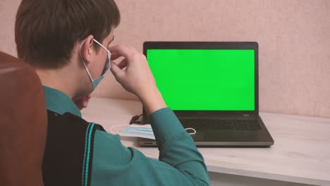 un hombre se pone una máscara de protección facial a sí mismo y al interlocutor por llamada de video y comienza a escribir en una computadora portátil, seguridad epidemiológica, trabajo remoto, pantalla verde