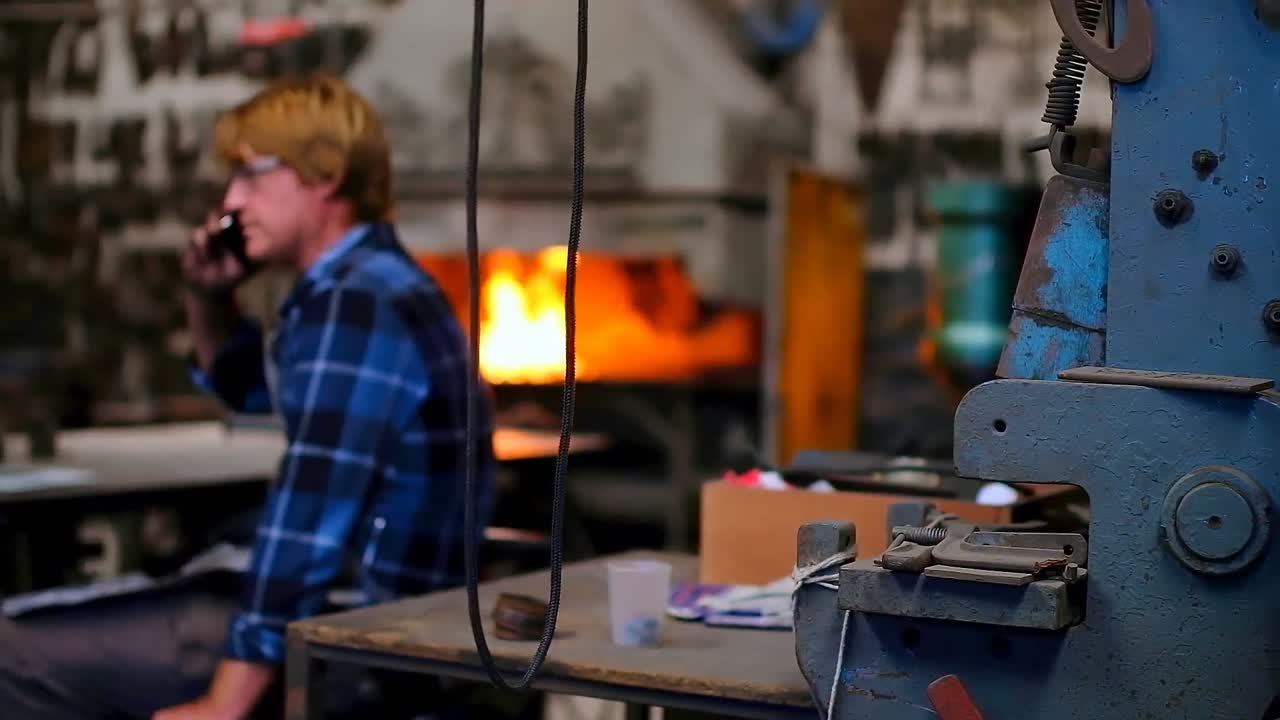 кузнец разговаривает по мобильному в мастерской 4k