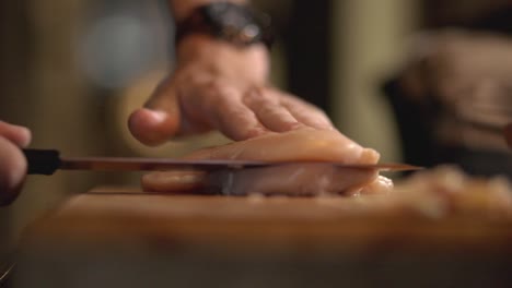 cook in the kitchen cutting the breast chicken fillet into half by a sharp knife