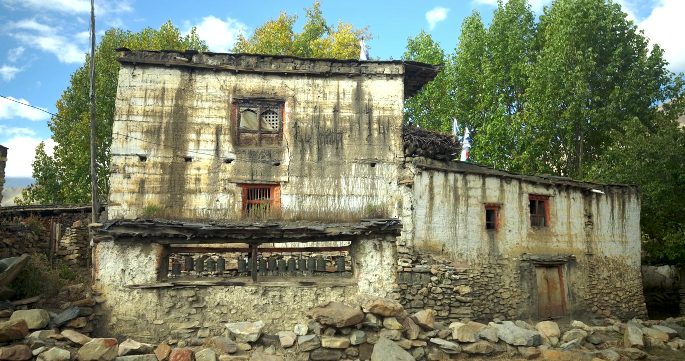 Circuito dell'Annapurna, Mustang, Nepal, un vecchio edificio in fango e pietra con ruote di preghiera sullo sfondo del fogliame autunnale con una disposizione di pietre a terra
