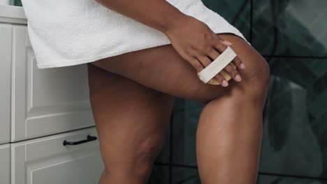 african-american woman doing peeling of her legs in the domestic bathroom.