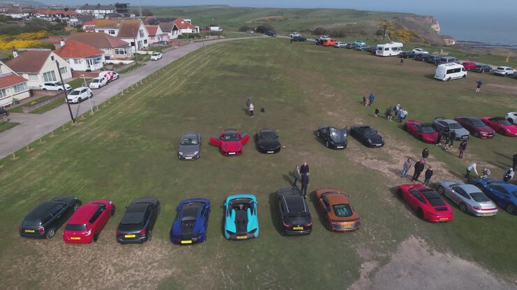 Aerial drone panning shot over rows of supercars parked outside Flamborough Head Lighthouse in Flamborough, UK at daytime