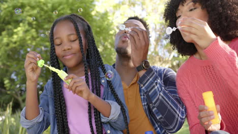 padres afroamericanos felices con la hija soplando burbujas en el jardín en casa, en cámara lenta