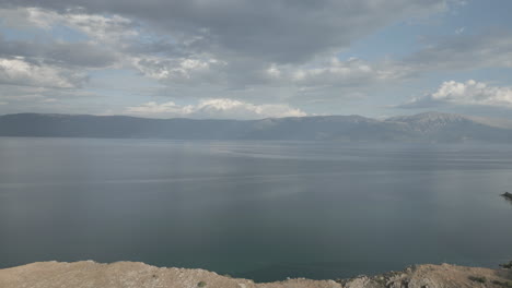 Drone-Volando-Hacia-Atrás-Sobre-El-Mar-En-Un-Día-Nublado-Con-Vistas-A-Macedonia-Revelando-La-Ciudad-De-Lin-Albania