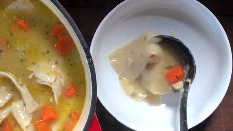 top view of ladling homemade chicken and dumplings into large white bowl