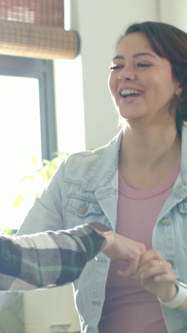 Video verticale: Donna in top rosa, camicia a quadri e giacca di jeans che si allunga, balla vicino alla finestra, con uno smartwatch.