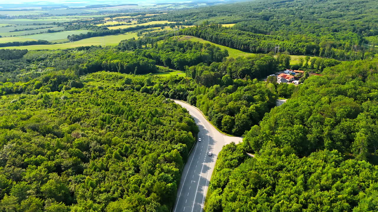 Winding road in green forest. A scenic road winds through vibrant green forests, surrounded by hills and fields, capturing nature's beauty in spring