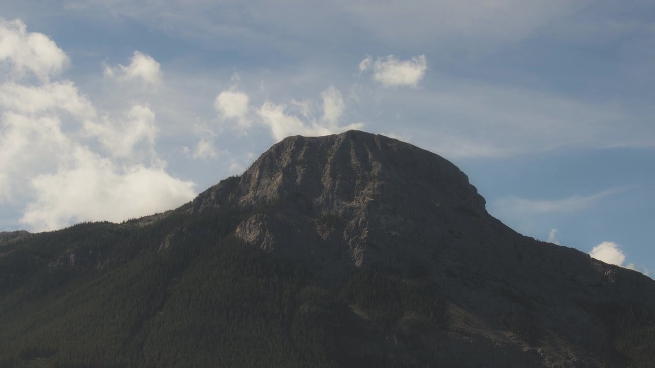 Høj tinde i Rocky Mountains mod blå himmel med hvide skyer.