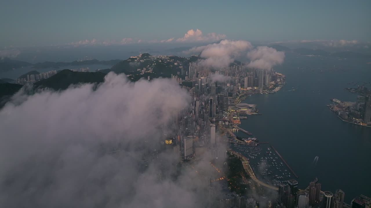 Lotnicze ujęcie z drona nad wzgórzem Braemer Hill w kierunku Causeway Bay w Hongkongu, podczas niebieskiej godziny, z nisko wiszącymi chmurami i kilkoma światłami miasta.