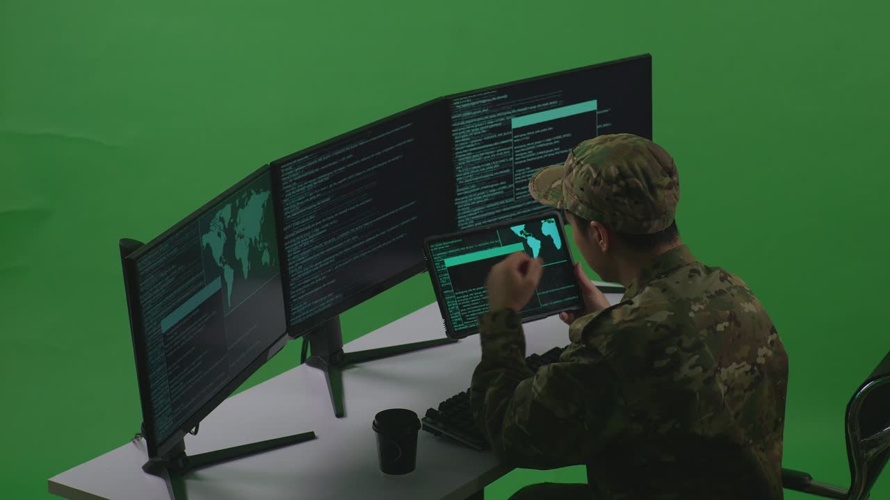 Side View Of Asian Man Soldier Developer Working With Tablet While Write Code With Multiple Computer Screens In Green Screen Studio
