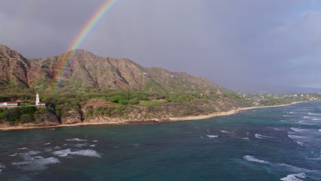 drone footage perfectly catching a rainbow against the volcanic mountains at diamond head lighthouse on the island of oahu near honolulu with the beautiful blue water of the pacific ocean