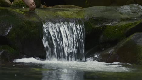 hand touching water of small waterfall in a forest