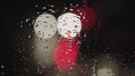 un primer plano de gotas de lluvia en el vidrio detrás del cual las luces de los coches que pasan crean una atmósfera colorida de tráfico nocturno