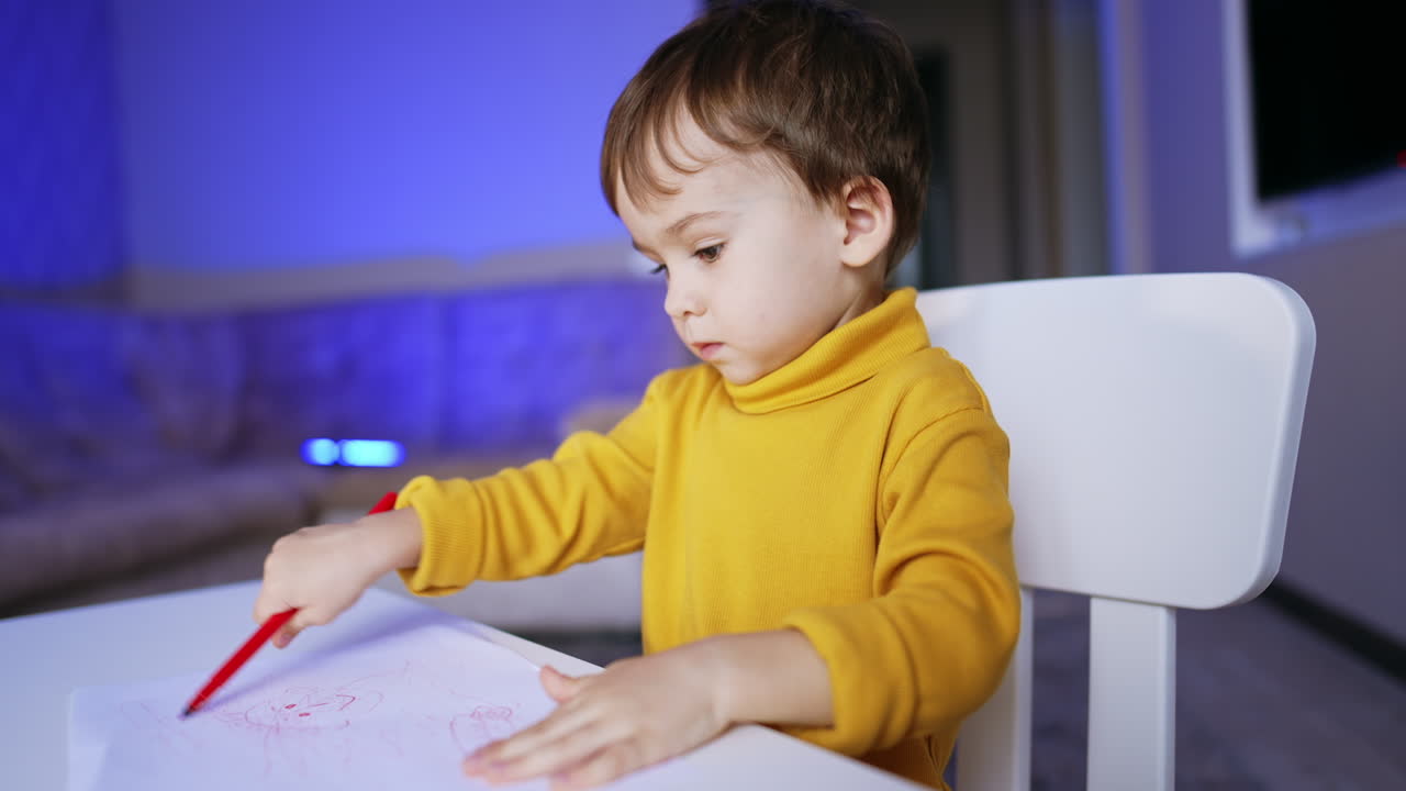Serious cute Caucasian kid focused on drawing. Portrait of a lovely baby boy having fun at home.
