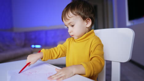 serious cute caucasian kid focused on drawing. portrait of a lovely baby boy having fun at home.