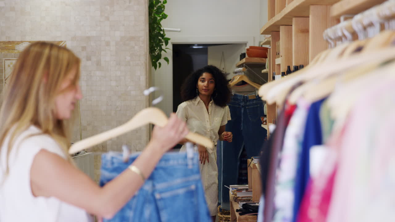 mujer comprando vaqueros en una tienda de moda pidiendo ayuda al asistente de ventas