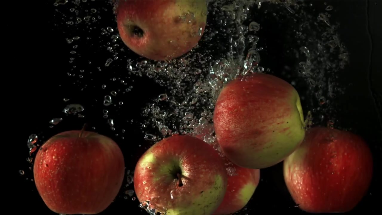Friske røde og grønne æbler falder ned i vand i slowmotion
