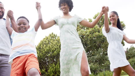 Happy-african-american-parents,-daughter-and-son-holding-hands-walking-in-garden,-slow-motion