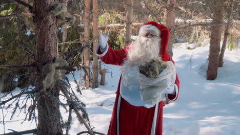 santa está parado en el bosque con un saco lleno de musgo en las manos y hablando con la cámara