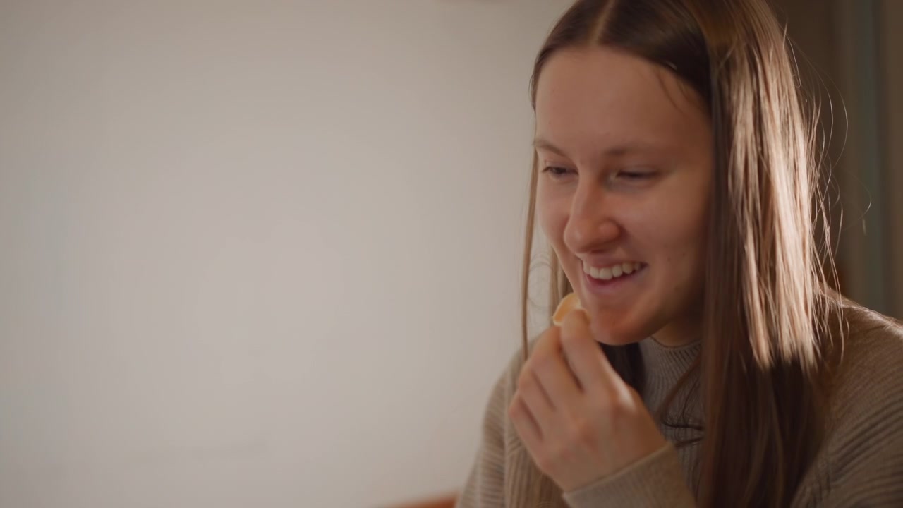 Donna sorride felicemente. Donna casual che assapora uno spuntino. Scena di cucina soleggiata con donna allegra. Momento autentico e spontaneo di una donna che si gode uno spuntino in un angolo soleggiato della cucina durante la routine mattutina.