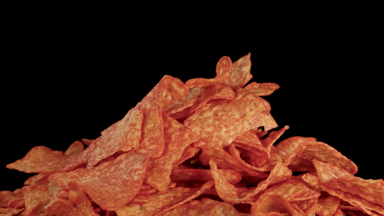Hand rotates seasoned nacho chips pile, close-up, dramatic lighting, black background, smooth camera movement