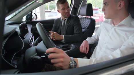 handsome young man buying a new car at the car showroom handsome young man buying a new car at the car showroom a wealthy young man is talking to a handsome sales manager in a luxury salon