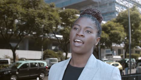 front view of a confident african-american businesswoman looking and speaking at the camera in the street