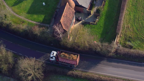 aerial view tracking an unrecognizable lorry along a road carrying agricultural materials