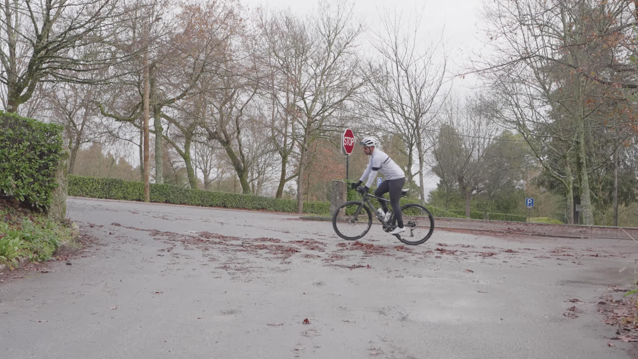 Ciclista che svolta su pavimentazione bagnata vicino a un segnale di stop durante il giorno.