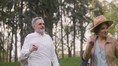 hombre y mujer de mediana edad bailando mientras sostiene copas de vino en el parque