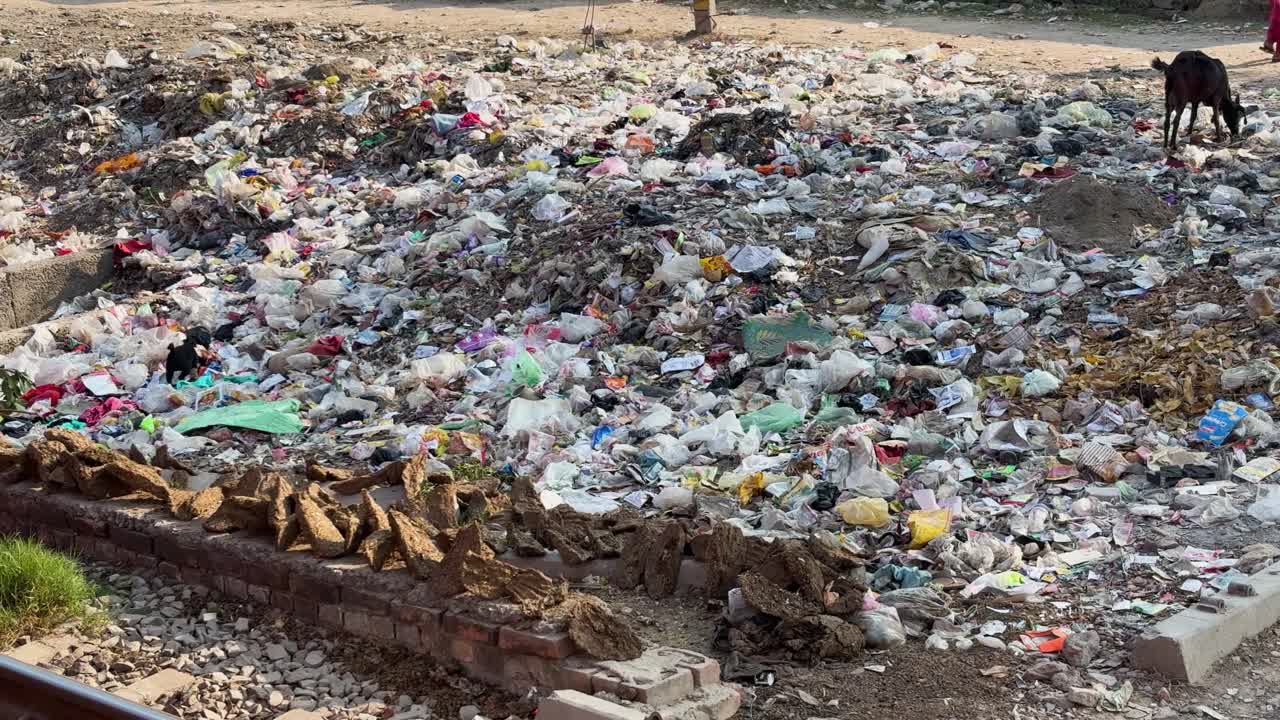 Aterro sanitário poluído perto da linha férrea com resíduos plásticos espalhados nos arredores da cidade.
