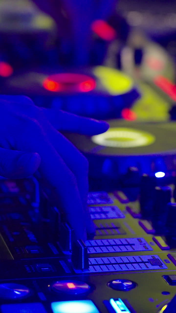 DJ Hand Adjusting Faders on Mixer in Nightclub with Colorful Lights