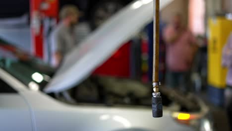 a day in the mechanic’s garage as people friends and family stand around broken broke down car chatting and talking in the shop, as focus is on compressed air hose hanging