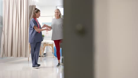 Caucasian-female-physiotherapist-helping-female-patient-with-prosthetic-leg-to-walk-at-rehab-center