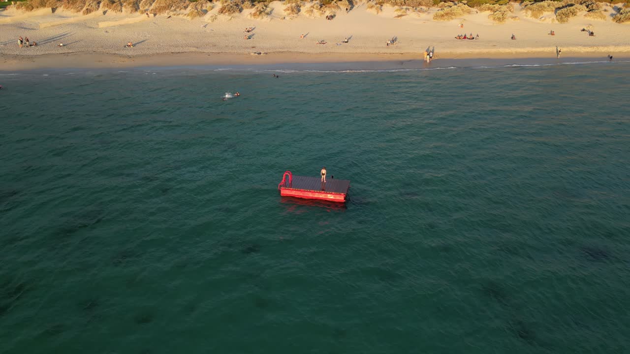 tomada aérea de dos amigos en una plataforma flotante en el océano divirtiéndose durante la puesta de sol dorada - playa sur de fremantle, australia occidental - vuelo en órbita de un avión no tripulado