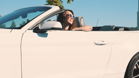 una mujer conduciendo un descapotable blanco.